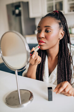 Home portrait of african american woman putting on red lipstick 