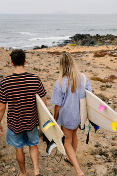 Seen from behind, a couple carries surfboards toward the ocean.