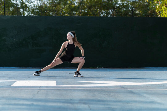 Woman in a lateral lunge stretch warming up on an outdoor court