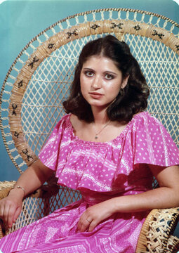 Woman posing in pink dress on a wicker chair
