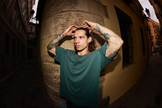 Young man poses against a wall in a narrow street during daytime