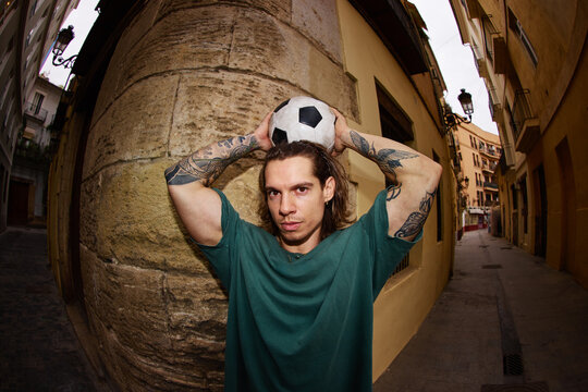 Man holds football ball in narrow street during afternoon