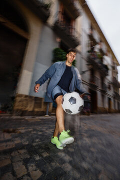 Man plays soccer in a street in an urban area during the day