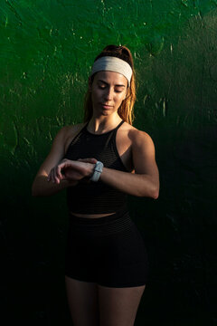 Urban runner checking her smartwatch against a green wall 