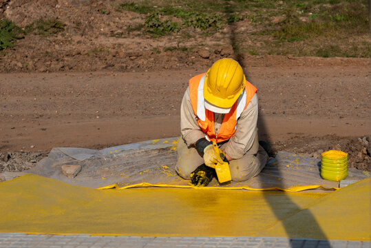 Worker squatting while painting pedestrian access ramp with yellow safety paint