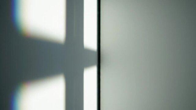 Abstract shadow from a window creates a cross shape and light reflections on a white wall