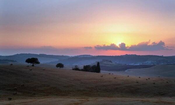 Sunset timelapse over harvested field with straw bales, rolling hills landscape in Tuscany, Italy