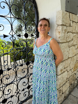 Senior Woman Stands by Ornate Gate in Outdoor Setting With Greenery
