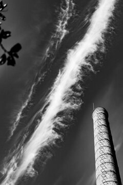 Tall chimney under cloudy sky with streaks of clouds above