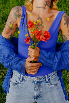 Woman holds flowers in a grassy field wearing a blue swimsuit
