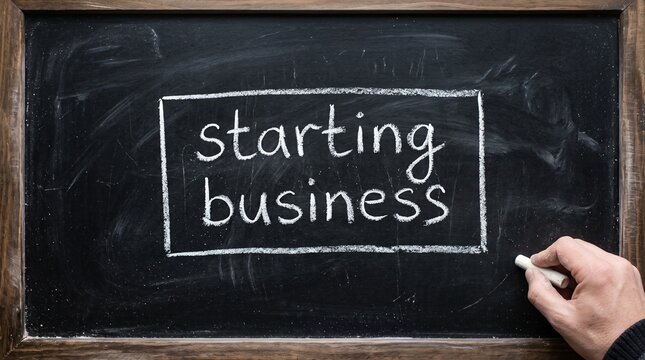 Human hand holds a piece of white chalk, drawing a rectangle around the words "starting business" written on a dark chalkboard.
