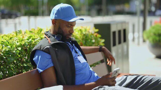 Delivery courier checking shipment updates and assigned orders on a smartphone while taking a short break outdoors between deliveries.