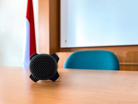 Close-up of a black handheld microphone resting on a wooden classroom table, ready for presentations, lectures, seminars, meetings, and public speaking events.