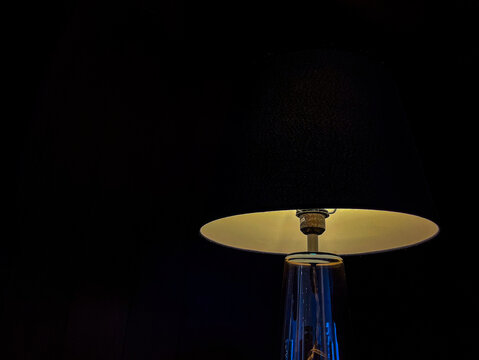 Modern table lamp glowing against a dark background, creating a warm minimalist atmosphere with elegant lighting, clean composition, and dramatic contrast for interior design concepts.