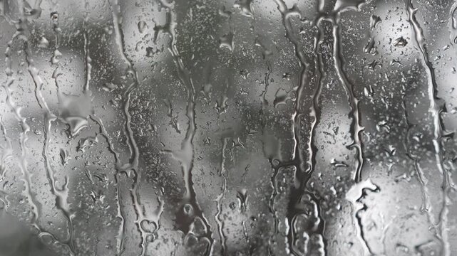Macro view of heavy streams of rainwater running down a wet glass window pane during a storm, creating a moody and emotional atmosphere on a rainy day.