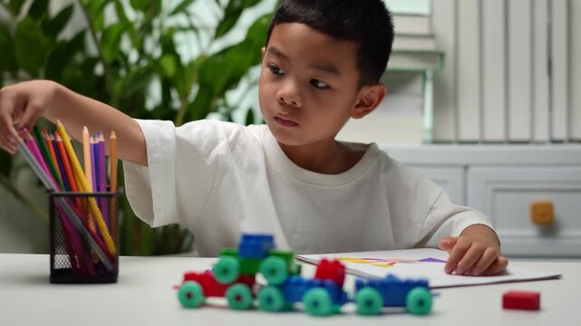 Focused young child drawing with colored pencils at home, encouraging creativity, imagination, fine motor skills, concentration and early childhood learning in a bright educational setting.