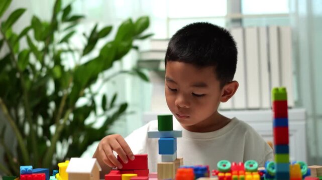 Focused young child building with colorful wooden blocks at home, promoting creativity, problem-solving, fine motor skills, concentration and early childhood learning in a bright playroom.