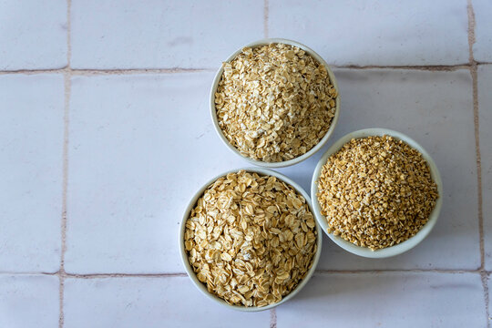 Instant, steel cut and old fashion oats in white ceramic bowl on a tile surface 