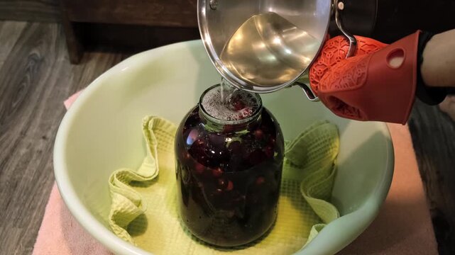 A man canning cherry compote using a manual seaming machine to seal a large glass jar with metal lid. Home canning, food preservation, traditional kitchen, winter storage preparations. A Can Seamer.