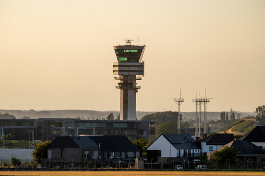 The air traffic control tower of Brussels Airport rises above the treeline in Belgium at golden hour, a key piece of aviation infrastructure against the evening sky.
