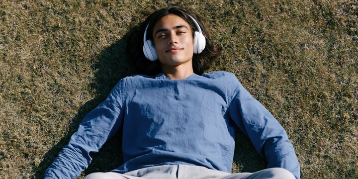 Young man lying on grass with headphones and arms out for meditation background and relaxation poster design