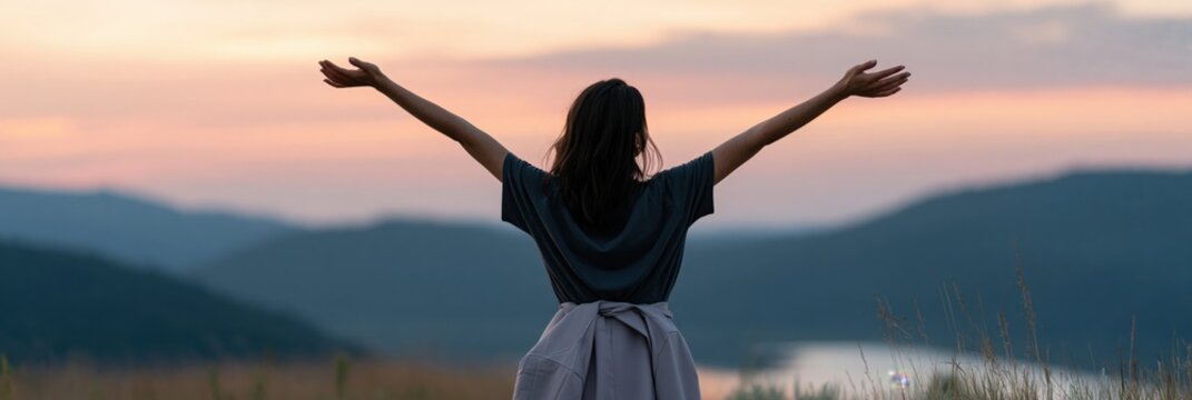 Back view woman with arms raised at mountain sunset overlooking a valley for peaceful wallpaper and nature background