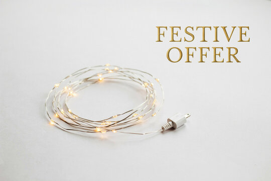 A coiled strand of delicate warm white glowing LED fairy string lights with a small white USB power plug connector lies neatly arranged for decoration on a bright clean plain surface