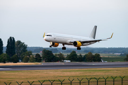An airliner flies low on short final over the runway threshold at Brussels Airport in Belgium in warm evening light before touchdown.