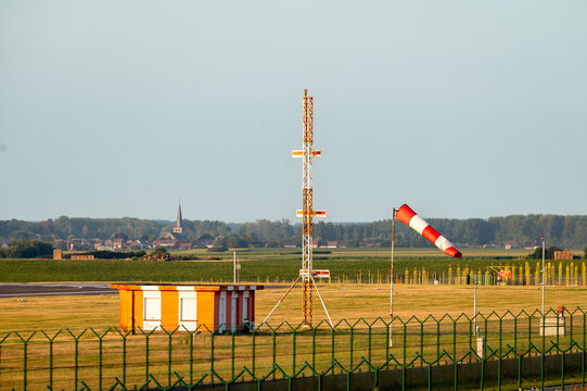 Approach lighting masts and an orange windsock line the grassy approach path to the runway at Brussels Airport in Belgium in golden evening light.