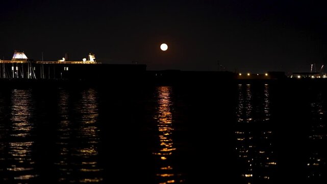A bright full moon shines in the dark sky casting a shimmering reflection on the calm harbor water. Such a tranquil coastal atmosphere inspires romantic evening walks and peaceful nighttime meditation