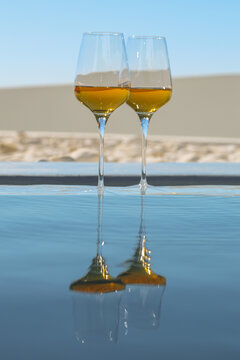 Two glasses of golden wine reflect perfectly on still water under the Santorini sun &mdash; a minimalist scene of Mediterranean elegance.