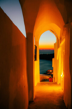 A glowing archway frames the Aegean Sea at twilight in Santorini, Greece &mdash; warm light and Cycladic curves create a timeless Mediterranean mood.