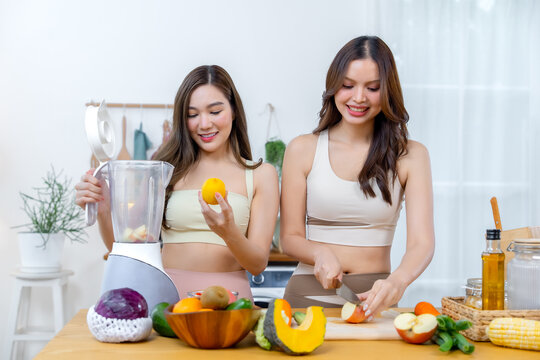 Smiling women using a blender while preparing colorful fresh ingredients in a home kitchen representing clean eating balanced nutrition healthy recipes and joyful friendship.
