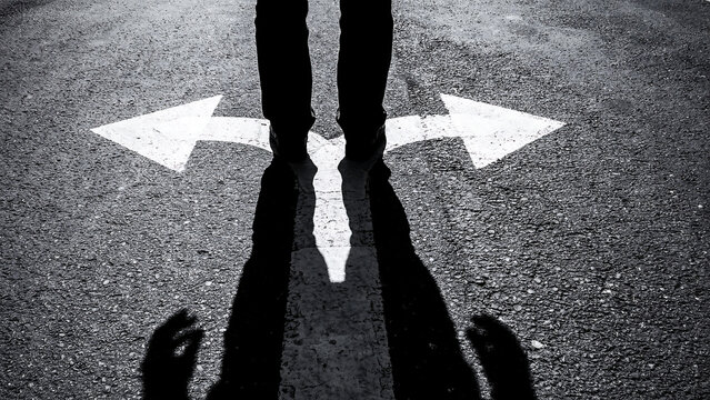 Business person standing at a fork in the road choosing between two directions conceptual metaphor for professional career path decisions decision direction crossroads lifestyle uncertainty