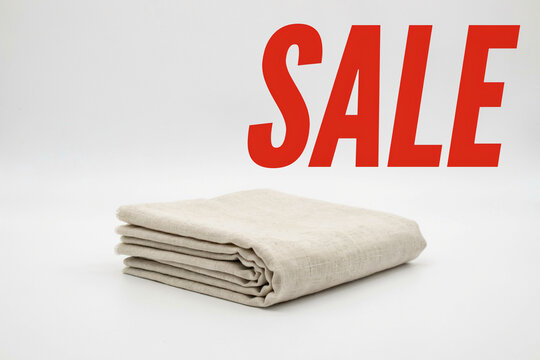 A neat stack of light beige natural linen fabric cloth textiles for clothing home decor or craft projects with a prominent bright red SALE sign indicating a discount promotion opportunity