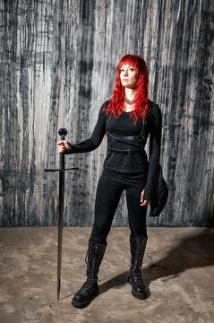 Dark fantasy redhaired woman with sword stands against grunge wall