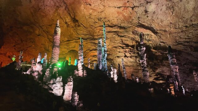 Underground limestone cave with tall stalagmites illuminated by artificial lighting. Geological rock formation inside cavern for exploration and nature education.