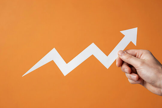 Hand holding white zigzag arrow against orange background with business increase financial progress performance marketing achievement improvement analysis management corporate strategy
