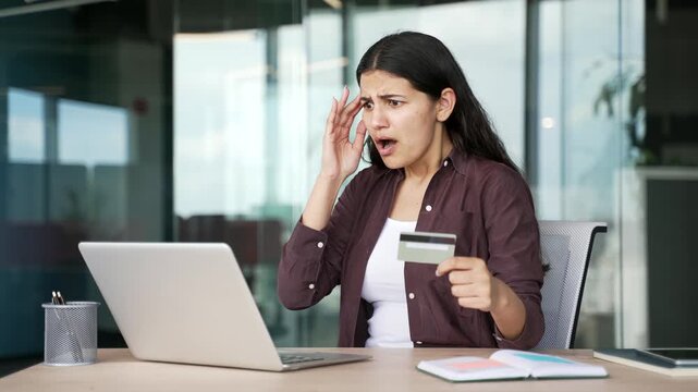 Shocked young businesswoman receives notification about blocked bank account holding credit card working on laptop in office. Worried female customer faces payment failure, unexpected banking problem.