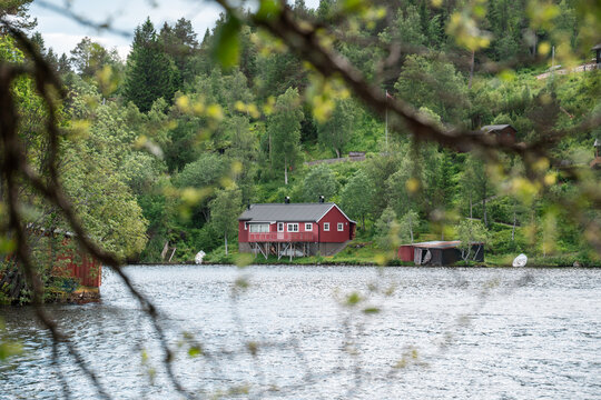 Red wooden cabin on the shore of a forest lake in Norway