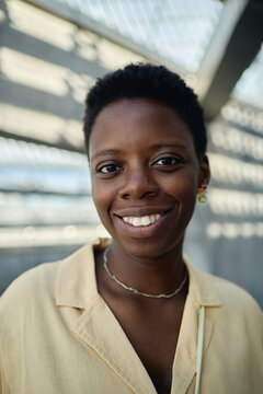 Vertical portrait of young Black woman smiling at camera, conveying confidence and approachable identity in urban setting. Useful for diversity marketing, personal branding