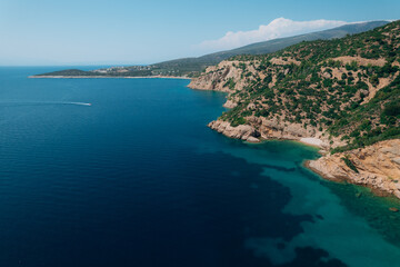 Naklejka premium Aerial drone view of a crystal clear turquoise bay on Thassos Island, Greece, with swimmers, paddleboards and a sandy beach surrounded by rocky coastline on a sunny summer day. 