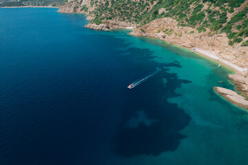 Aerial view of a fast motor yacht cutting through crystal-clear blue water. Vibrant textures, dynamic waves, powerful motion create the perfect visual for themes of luxury, freedom, vacation. © Miha Creative