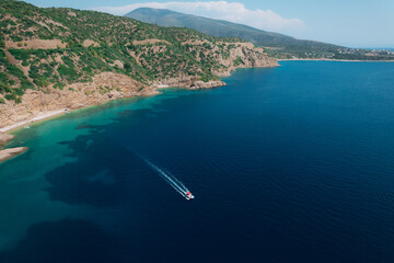 Aerial view of a fast motor yacht cutting through crystal-clear blue water. Vibrant textures, dynamic waves, powerful motion create the perfect visual for themes of luxury, freedom, vacation. © Miha Creative