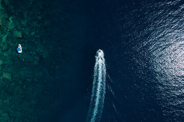 Aerial view of a fast motor yacht cutting through crystal-clear blue water. Vibrant textures, dynamic waves, powerful motion create the perfect visual for themes of luxury, freedom, vacation. © Miha Creative