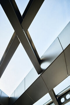 Vertical shot of modern architectural ceiling featuring intersecting steel beams and skylight panels, creating abstract corporate design background. For business branding or construction marketing