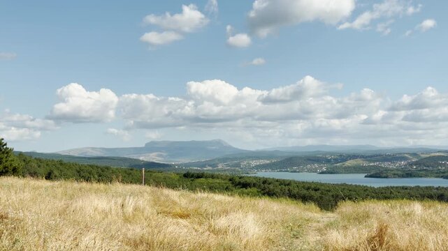 Mount Chatyr-Dag stands majestic on the horizon of Simferopol, Crimea. Golden fields and a calm blue lake rest under fluffy clouds, bringing a joyful feeling of peaceful freedom.
