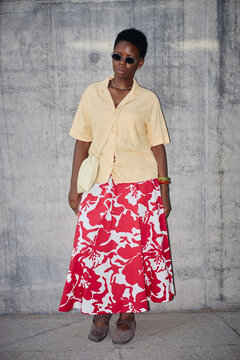 Vertical shot of young Black woman standing against concrete wall, wearing sunglasses and posing with confident urban style. Suitable for fashion marketing, personal branding, vertical