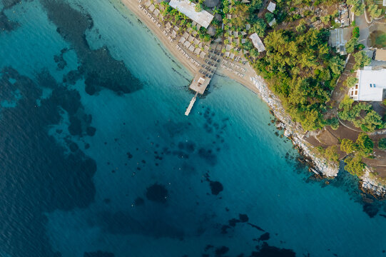 Aerial drone of a peaceful beach in Thassos, Greece, featuring transparent turquoise water, paddleboards, swimmers and a beautiful Mediterranean coastline.