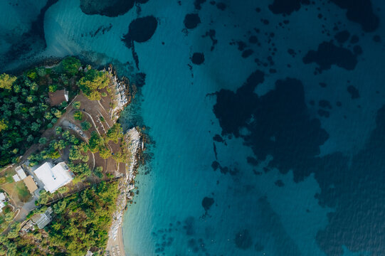 Aerial drone of a peaceful beach in Thassos, Greece, featuring transparent turquoise water, paddleboards, swimmers and a beautiful Mediterranean coastline.
